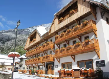 Bâtiment blanc avec balcons en bois, sol et sapins enneigés